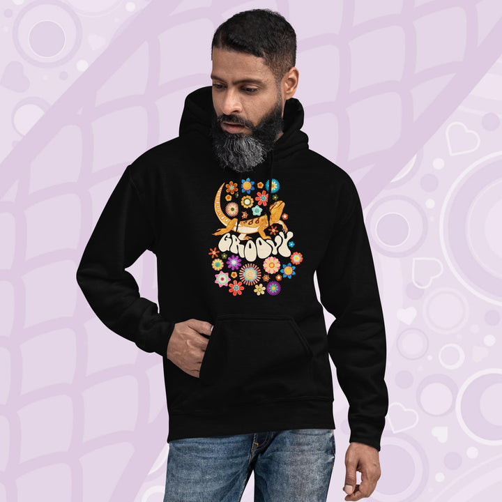 A black hooded sweatshirt with a graphic of a bearded dragon with the word "Groovy" in a retro font surrounded by colorful flowers in a 70's inspired theme.