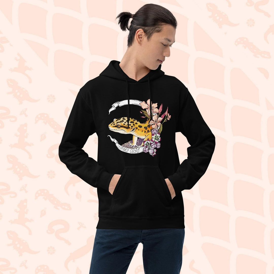 A black hoodie with a white banner wrapping around a design featuring a bright yellow leopard gecko, pink and purple flowers, and the text "Leopard Gecko" along the bottom of the white banner.