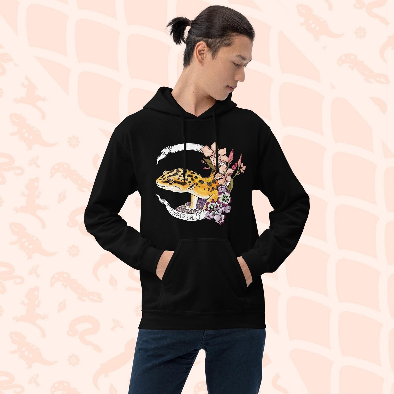 A black hoodie with a white banner wrapping around a design featuring a bright yellow leopard gecko, pink and purple flowers, and the text "Leopard Gecko" along the bottom of the white banner.