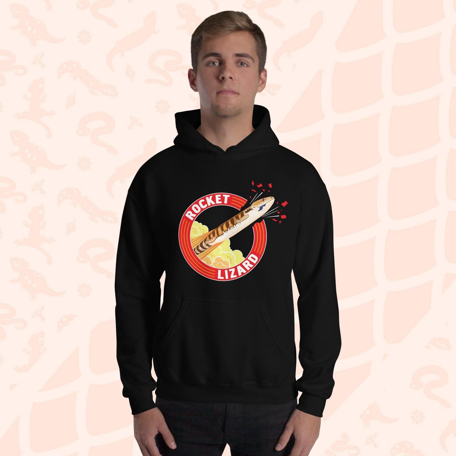 A man wearing a black hooded sweatshirt with a red circle graphic with text saying "Rocket Lizard." In the center of the graphic is a cartoon blue tongue skink shooting upward and breaking through the red outer circle with the text. It's tongue is hanging out of it's mouth as it rockets out with a plume of yellow and orange clouds billowing behind it. The hoodie has a front pocket.