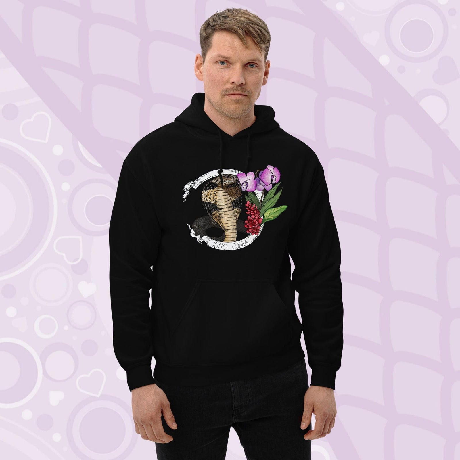 A man wearing a black hooded sweatshirt with a graphic of a king cobra with pink orchids  and smaller red flowers on the right side of the design. The text "KING COBRA" is printed below the snake. The hoodie has a front pocket.