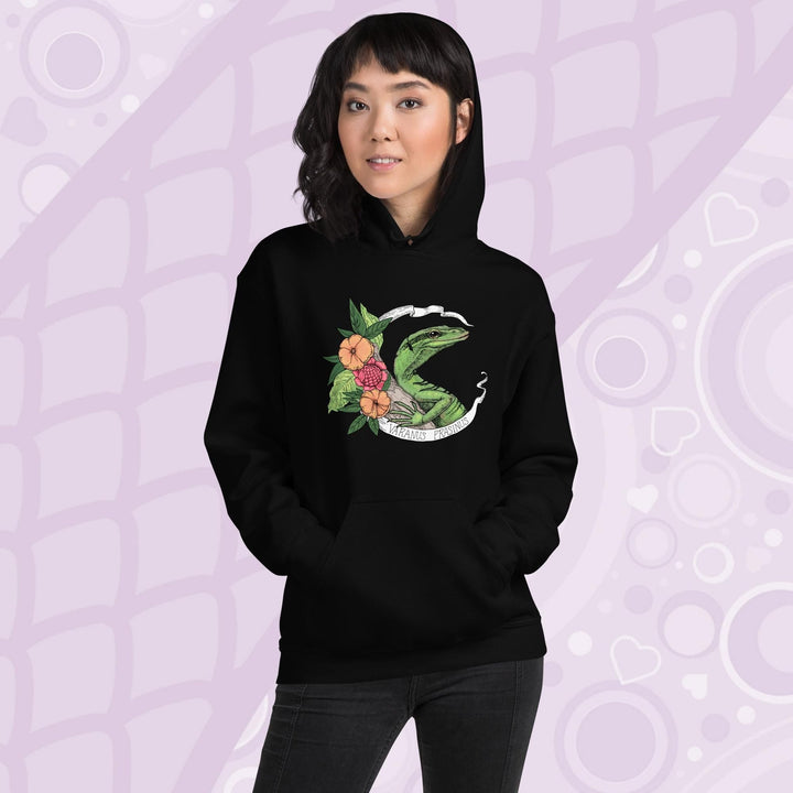 A woman wearing a black hoodie with a graphic of a slender green tree monitor lizard with orange and warm orange red flowers and the text "Varanus Prasinus" on a white banner surrounding the reptile. The hoodie has a front pocket.