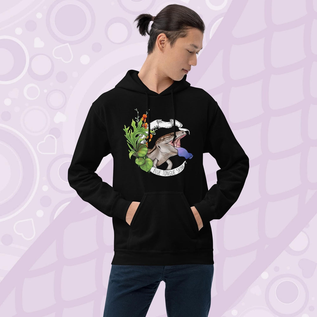 Man wearing a black hooded pullover sweatshirt with a graphic of a blue-tongued skink, it's mouth open and it's blue tongue flashing in a classic defensive posture. The lizard is surrounded by green leaves and flowers. The text "Blue Tongue Skink" is written on a white banner.