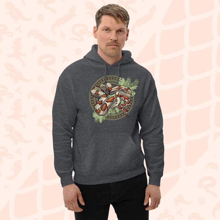 A man wearing a dark grey hooded sweatshirt with a graphic print of a red tailed boa constrictor snake with bold red's and brown markings. The snake is curled up in a circle made of patterned geometric shapes and with leafy green foliage beneath the snakes body. The hoodie has a front pocket.