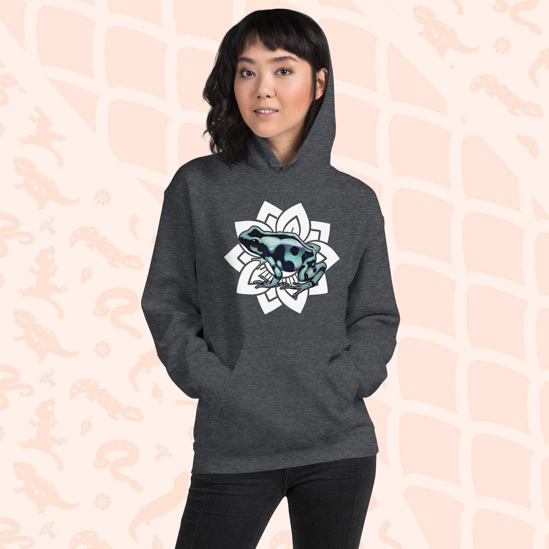 A woman wearing a dark grey hoodie with a white mandala design featuring a green and black poison dart frog. The hoodie is made of cotton and has a front pouch sewn on the front.