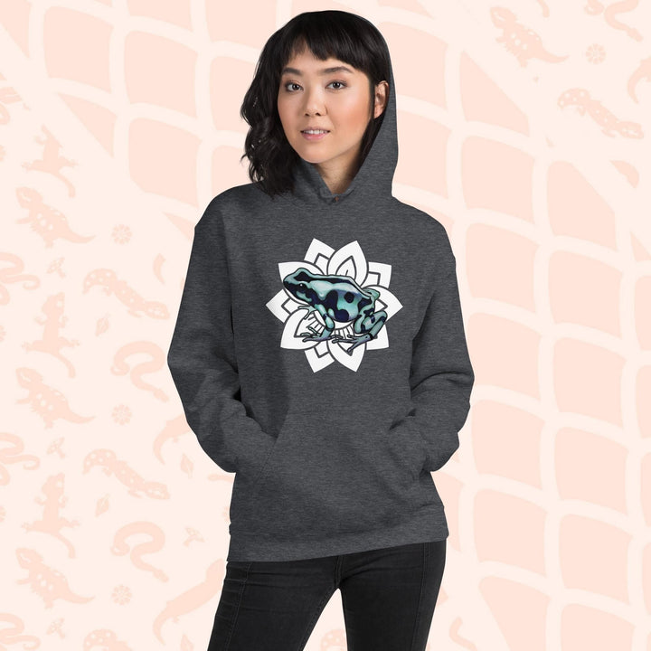 A woman wearing a dark grey hoodie with a white mandala design featuring a green and black poison dart frog. The hoodie is made of cotton and has a front pouch sewn on the front.