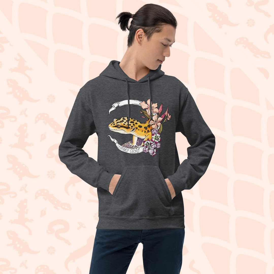 A dark grey hoodie with a white banner wrapping around a design featuring a bright yellow leopard gecko, pink and purple flowers, and the text "Leopard Gecko" along the bottom of the white banner.