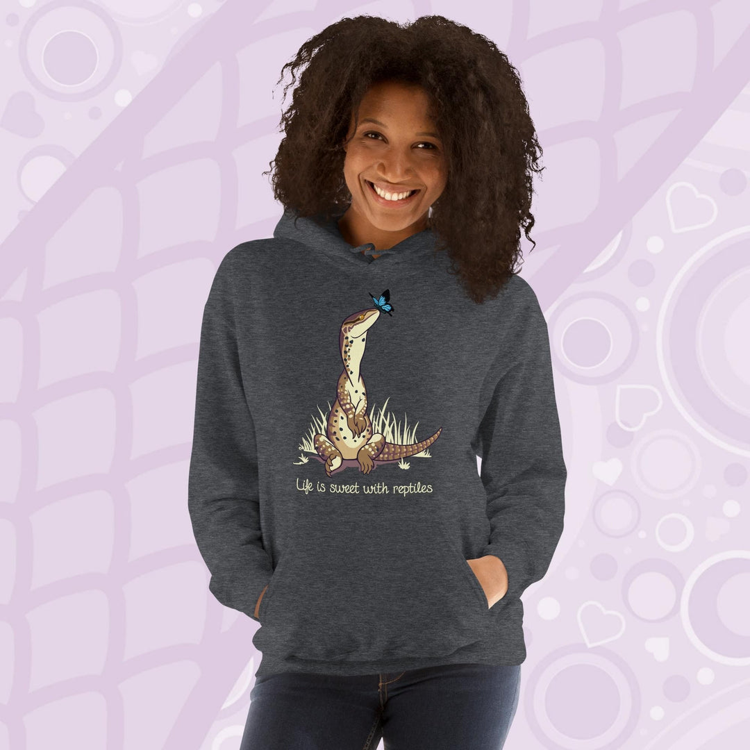 A smiling woman wearing a dark grey hoodie with a front pouch and a cartoon graphic on the front of an argus monitor lizard sitting in grass with a little butterfly on it's nose. The text underneath says, "Life is sweet with reptiles."