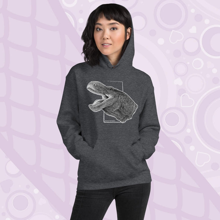 A woman wearing a grey hooded sweatshirt with a graphite illustration of a head portrait of a crocodile monitor reptile with its mouth open. The illustration is framed by a white rectangle and the text "Varanus Salvadorii" is below the image. The hoodie has a front pocket.
