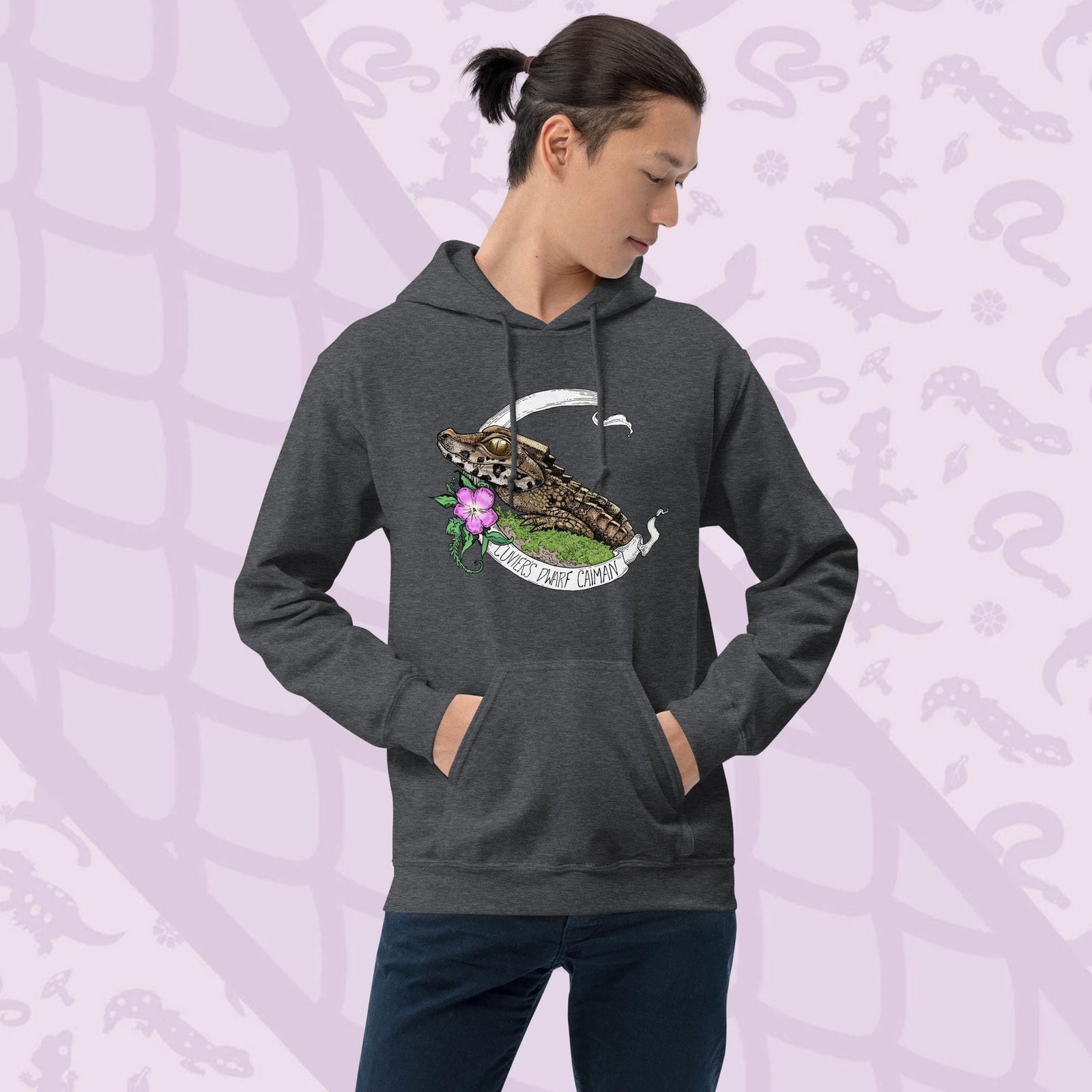 Dark Grey hooded sweatshirt featuring a detailed illustration of a caiman with a flower and banner. The banner reads "Cuviers Dwarf Caiman". The caiman is brown and green, with a pink flower and green foliage. The sweatshirt has a front pocket and a drawstring hood.