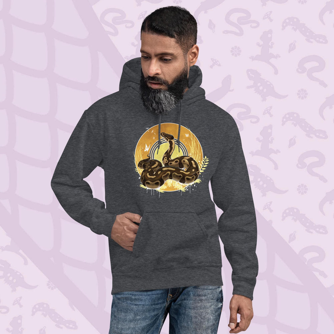 Grey hoodie with a graphic of a normal ball python snake with it's amber and brown colored scales coiled in a circle with it's head lifted up and looking upward. Behind it is a series of circles with golden hues and tall amber grasses with white butterflies and seeds floating on the wind.