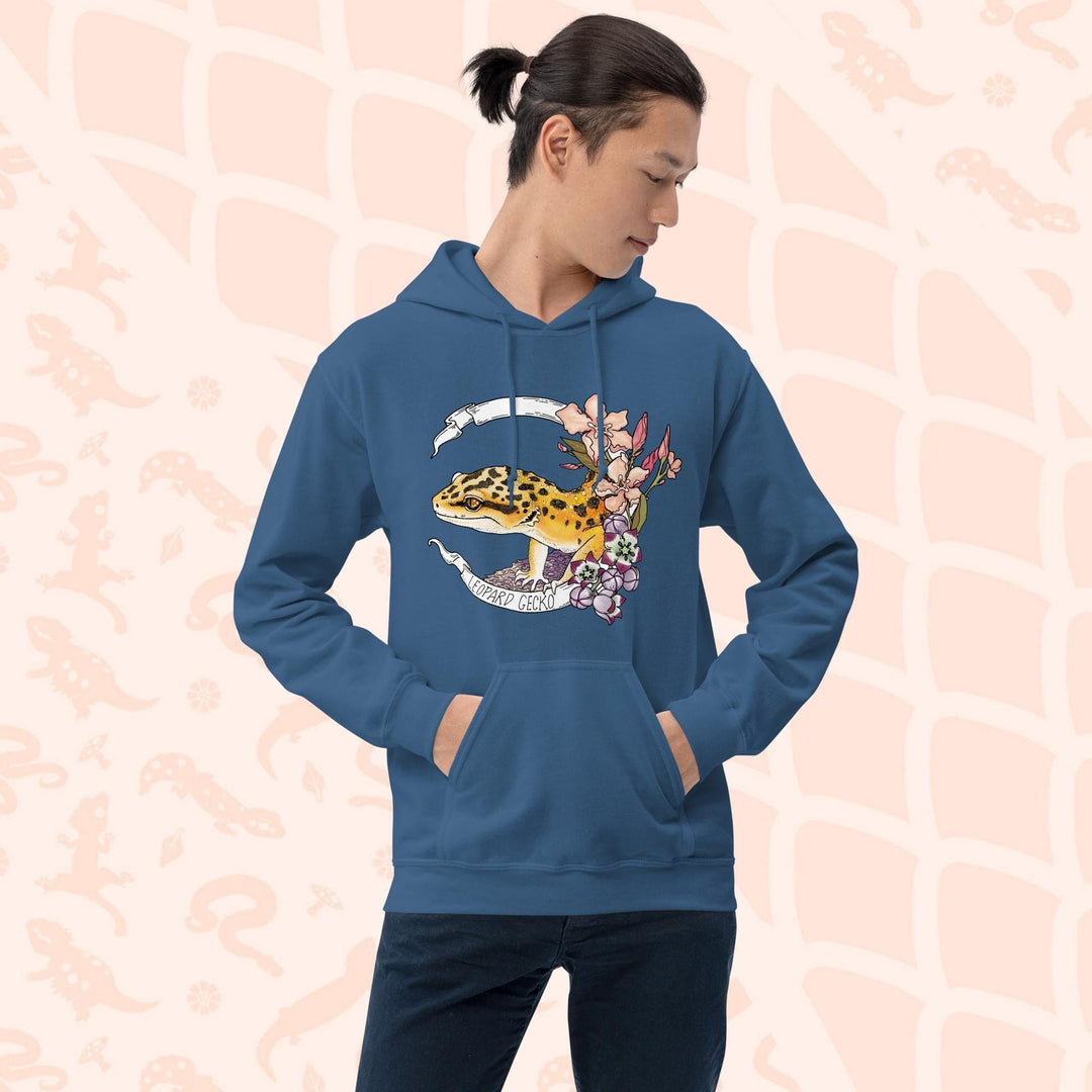 A neutral blue hoodie with a white banner wrapping around a design featuring a bright yellow leopard gecko, pink and purple flowers, and the text "Leopard Gecko" along the bottom of the white banner.