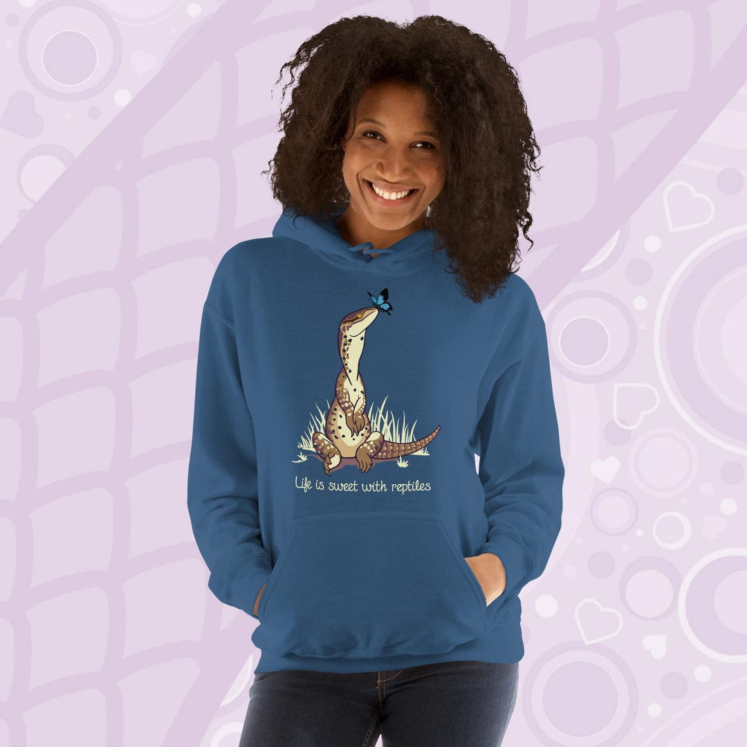 A smiling woman wearing a neutral blue hoodie with a front pouch and a cartoon graphic on the front of an argus monitor lizard sitting in grass with a little butterfly on it's nose. The text underneath says, "Life is sweet with reptiles."