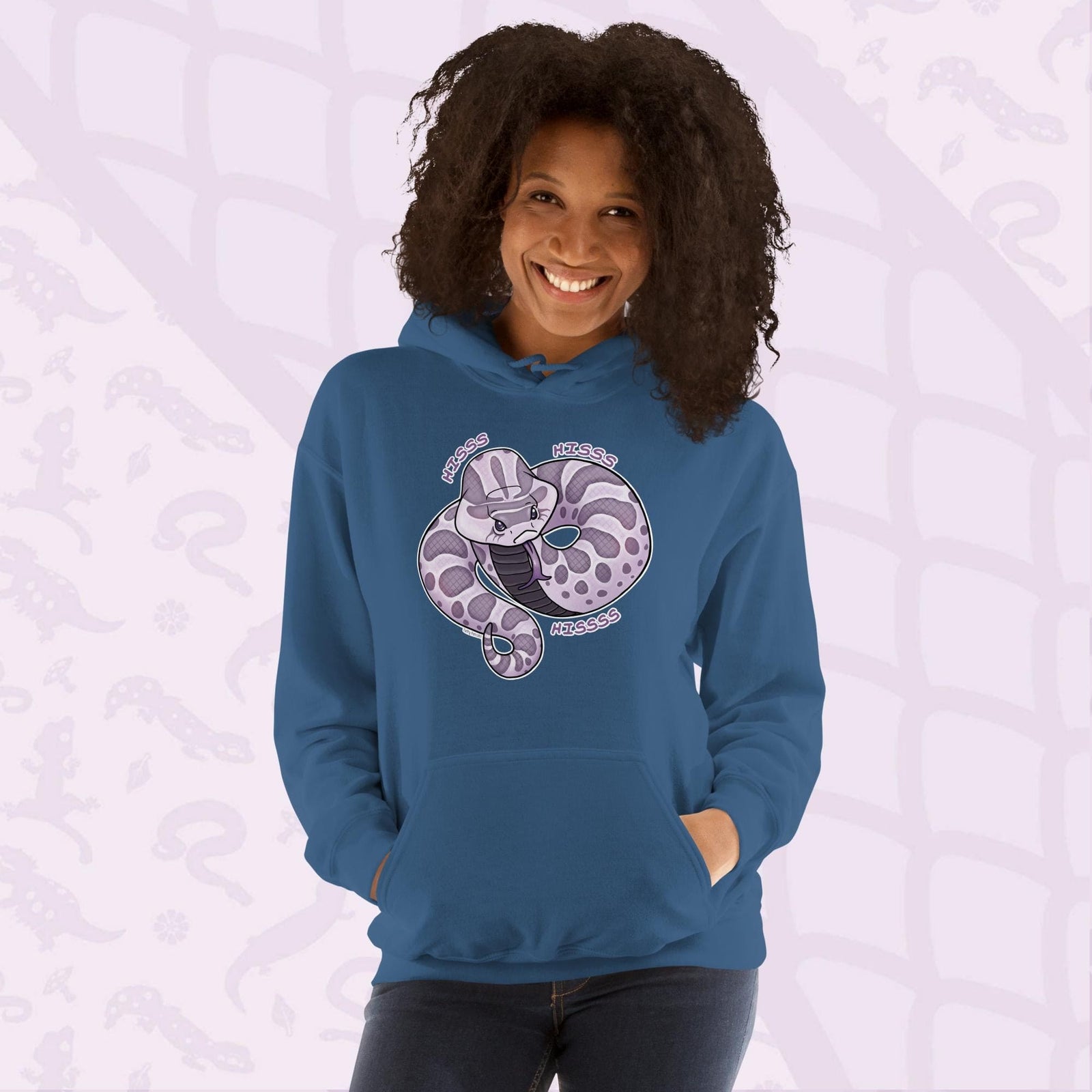 A woman wearing a neutral blue hoodie featuring a cartoon hognose snake design in shades of purple and gray. The snake is coiled and has the word "Hiss Hiss Hiss" printed around it. The hoodie has a front pocket and a hood.