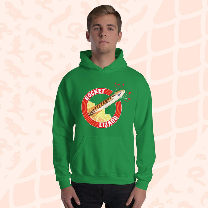 A man wearing a bright green hooded sweatshirt with a red circle graphic with text saying "Rocket Lizard." In the center of the graphic is a cartoon blue tongue skink shooting upward and breaking through the red outer circle with the text. It's tongue is hanging out of it's mouth as it rockets out with a plume of yellow and orange clouds billowing behind it. The hoodie has a front pocket.