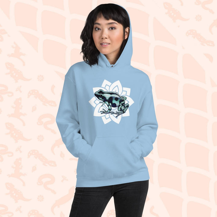 A woman wearing a light blue hoodie with a white mandala design featuring a green and black poison dart frog. The hoodie is made of cotton and has a front pouch sewn on the front.