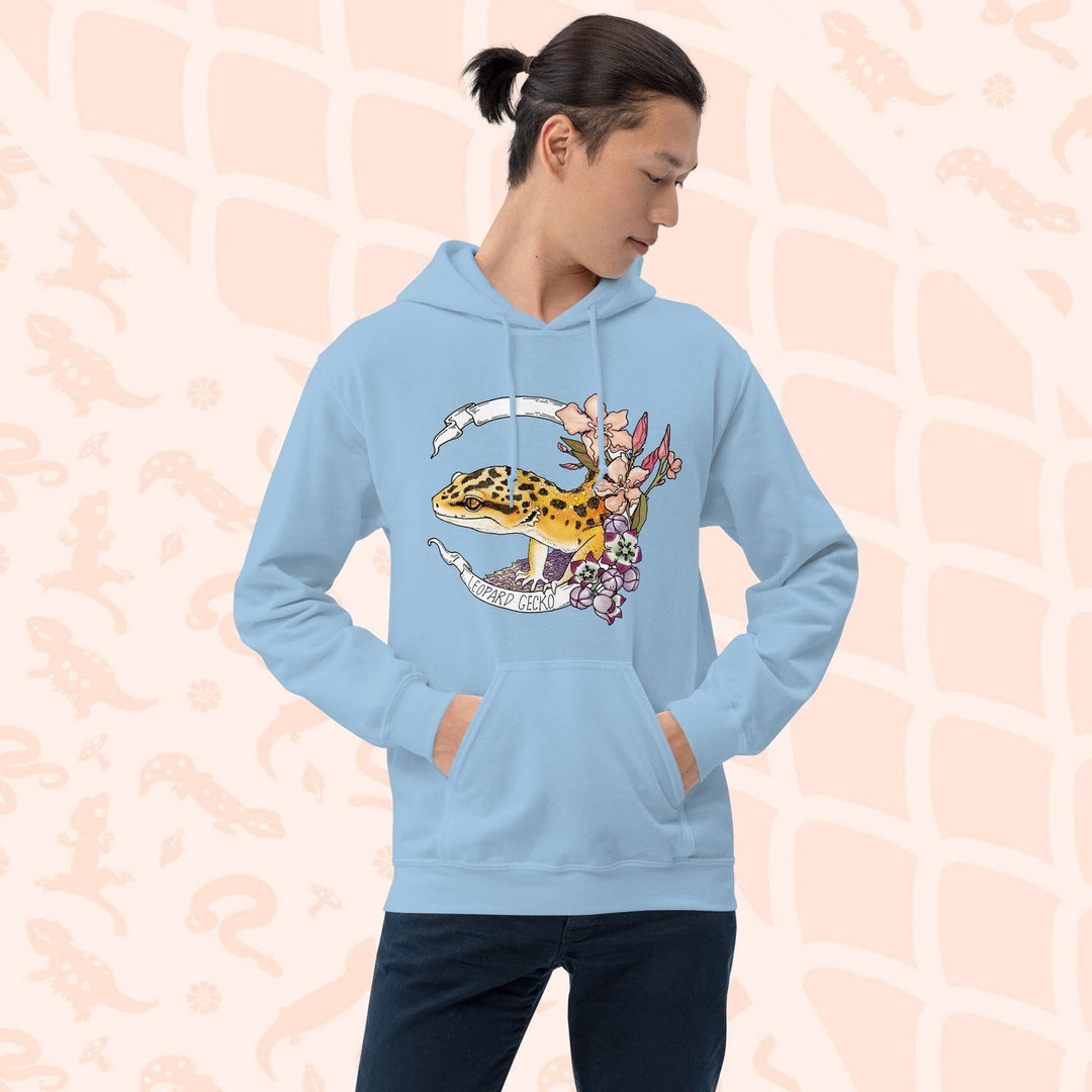 A light blue hoodie with a white banner wrapping around a design featuring a bright yellow leopard gecko, pink and purple flowers, and the text "Leopard Gecko" along the bottom of the white banner.