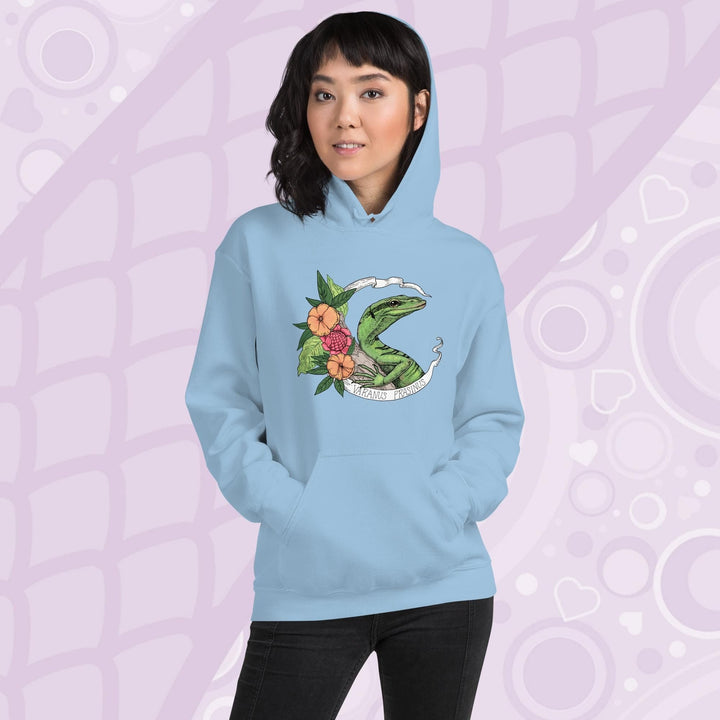 A woman wearing a soft light blue hoodie with a graphic of a slender green tree monitor lizard with orange and warm orange red flowers and the text "Varanus Prasinus" on a white banner surrounding the reptile. The hoodie has a front pocket.