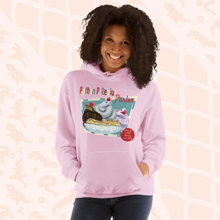 A soft pink hoodie with a retro-style graphic of a sundae with three ball pythons on top. The graphic says "Python P. Regius Parlor" and "Serving 2,000+ flavors since 1990".