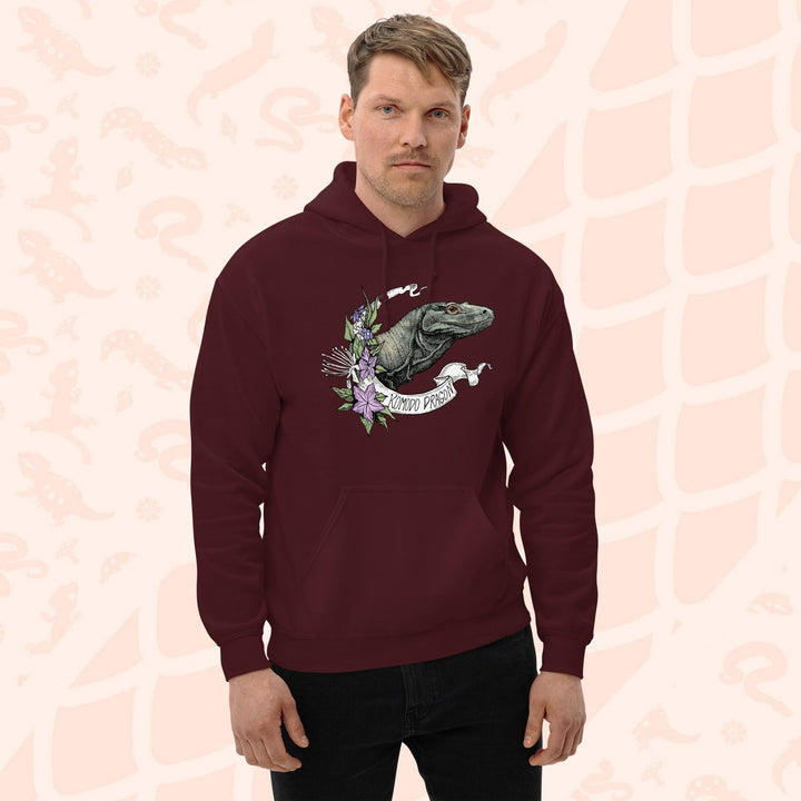 A dark red maroon hooded sweatshirt with a graphic print of a Komodo dragon with purple flowers and the text "Komodo Dragon" on the white banner framing the design. The hoodie has a front pocket.