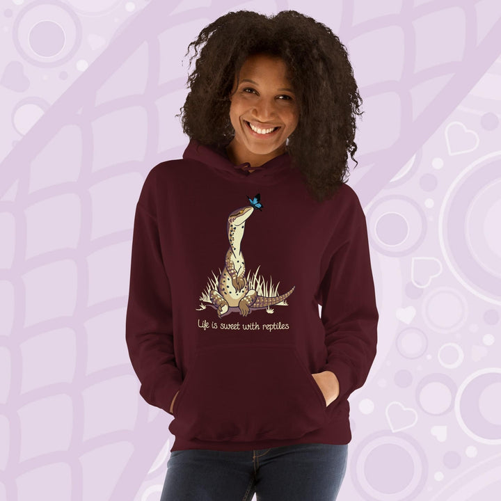 A smiling woman wearing a dark red maroon hoodie with a front pouch and a cartoon graphic on the front of an argus monitor lizard sitting in grass with a little butterfly on it's nose. The text underneath says, "Life is sweet with reptiles."
