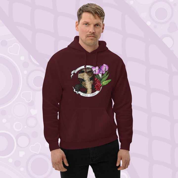 A man wearing a dark maroon red hooded sweatshirt with a graphic of a king cobra with pink orchids  and smaller red flowers on the right side of the design. The text "KING COBRA" is printed below the snake. The hoodie has a front pocket.