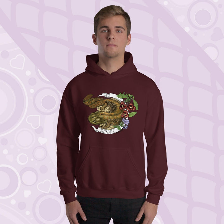 A man wearing a dark red maroon hoodie featuring a detailed illustration of a salamander with the text "HELLBENDER" in white. The design includes floral elements in red, green, and purple. The hoodie has a front pocket and a hood.