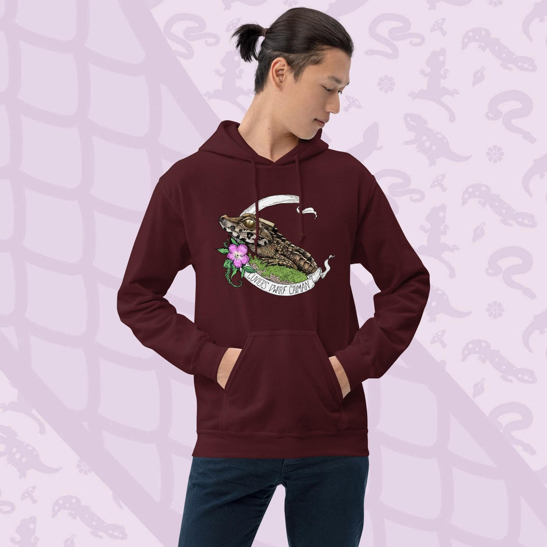 Dark red hooded sweatshirt featuring a detailed illustration of a caiman with a flower and banner. The banner reads "Cuviers Dwarf Caiman". The caiman is brown and green, with a pink flower and green foliage. The sweatshirt has a front pocket and a drawstring hood.