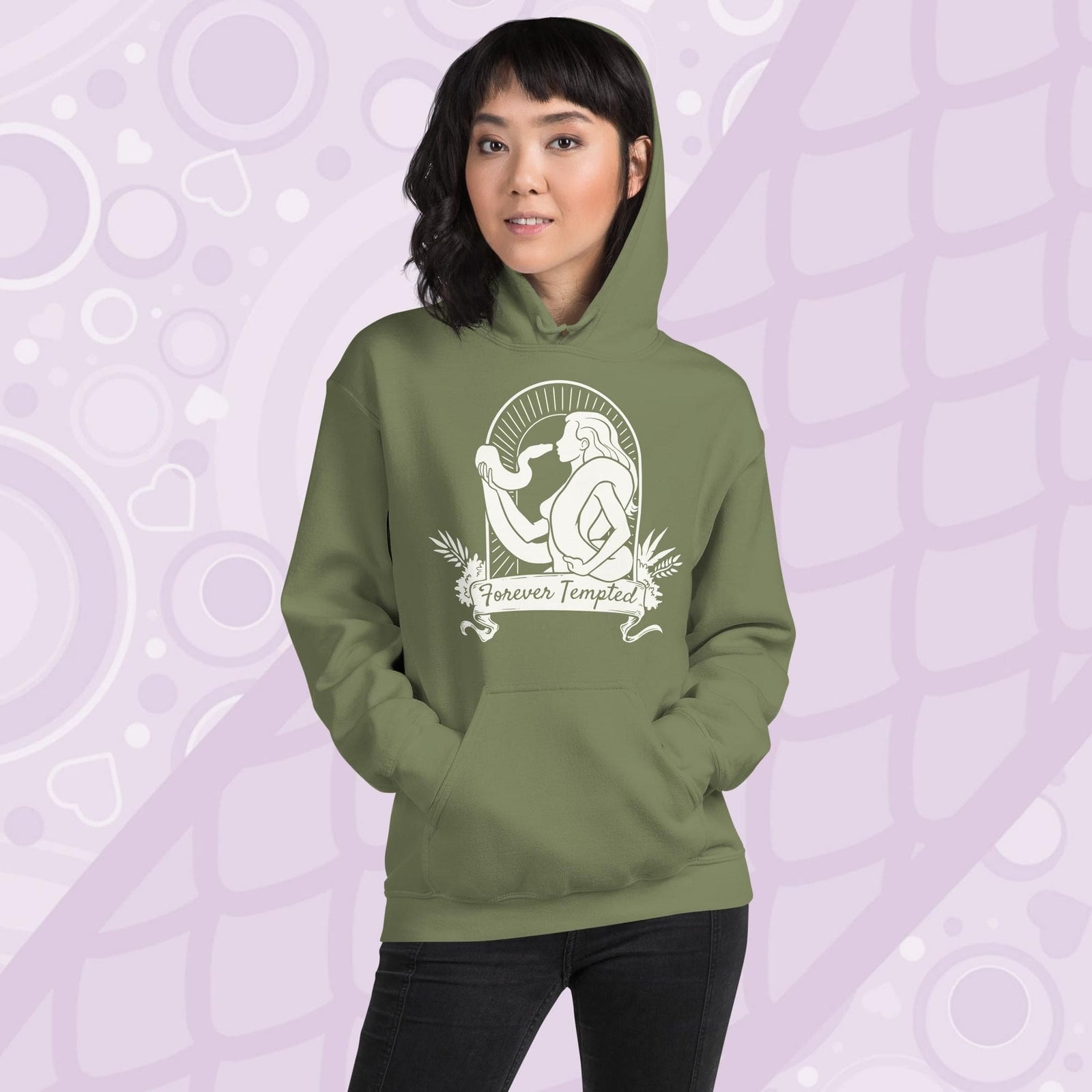 Woman wearing an olive green hoodie with a white graphic of a silhouetted woman with a snake wrapped around her. Her hand holds up the snakes head and they are staring at each other. The graphic is in an arch with the text "Forever Tempted" on a banner below.