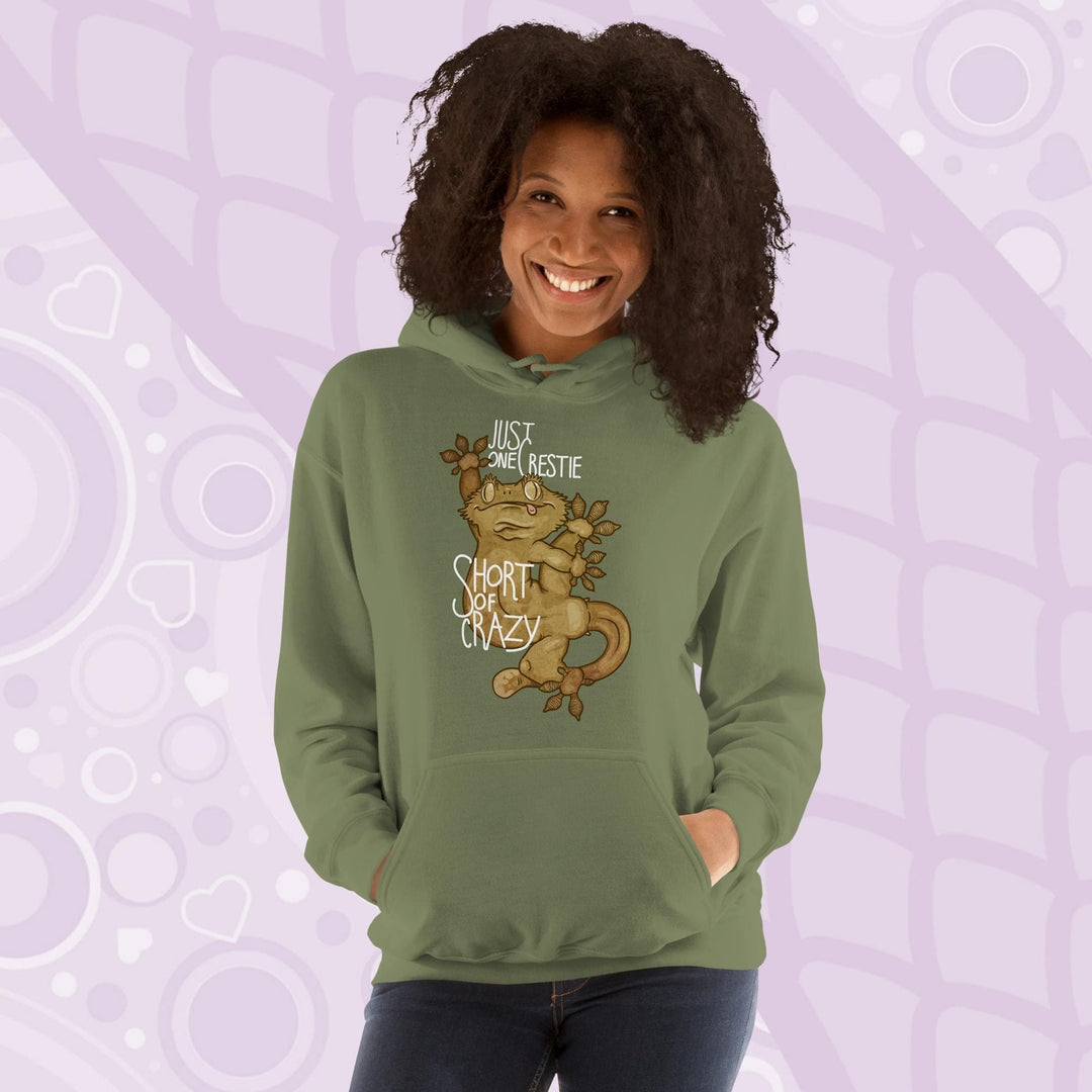 Woman wearing a olive green colored pullover hoodie with a goofy, cartoonish graphic of a crested gecko with it's legs contorted in many directions. The text, "Just one crestie short of crazy." is printed on the front.