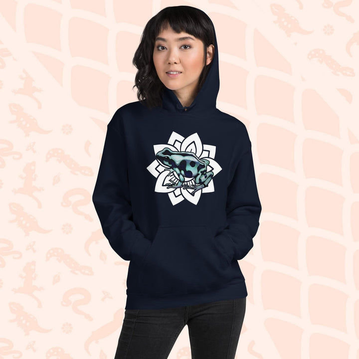 A woman wearing a dark navy blue hoodie with a white mandala design featuring a green and black poison dart frog. The hoodie is made of cotton and has a front pouch sewn on the front.