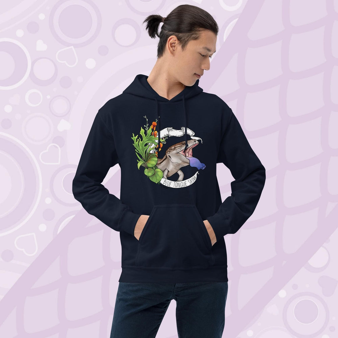Man wearing a navy blue hooded pullover sweatshirt with a graphic of a blue-tongued skink, it's mouth open and it's blue tongue flashing in a classic defensive posture. The lizard is surrounded by green leaves and flowers. The text "Blue Tongue Skink" is written on a white banner.