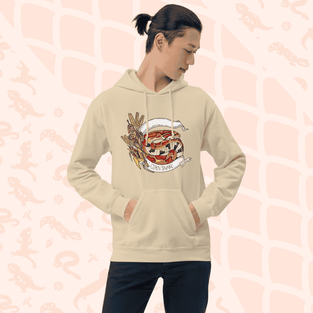 A man wearing beige pull over hoodie with a vibrant orange colored rat snake coiled in-between a white banner stating the species and glass corn on the left side.