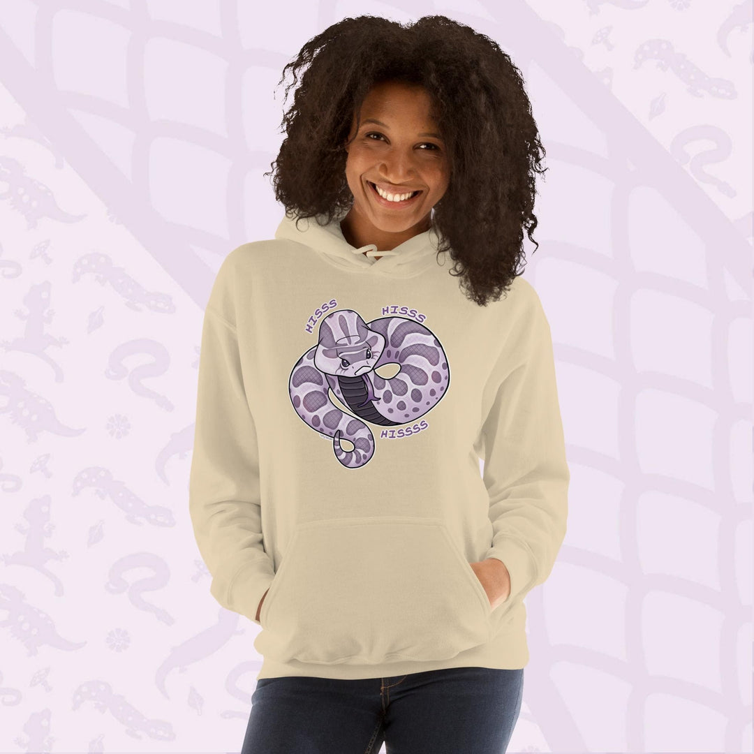 A woman wearing a soft cream hoodie featuring a cartoon hognose snake design in shades of purple and gray. The snake is coiled and has the word "Hiss Hiss Hiss" printed around it. The hoodie has a front pocket and a hood.
