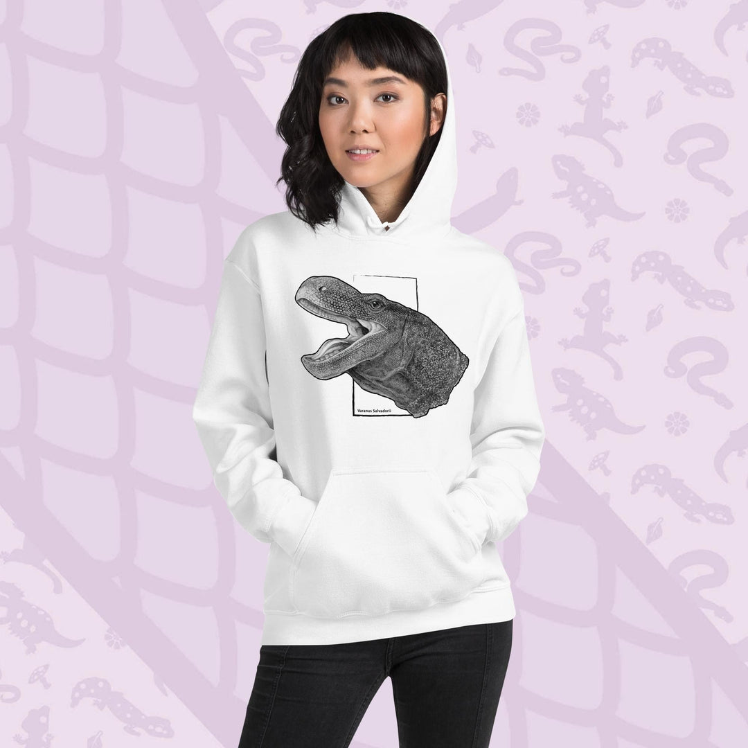 A woman wearing a white hooded sweatshirt with a graphite illustration of a head portrait of a crocodile monitor reptile with its mouth open. The illustration is framed by a white rectangle and the text "Varanus Salvadorii" is below the image. The hoodie has a front pocket.