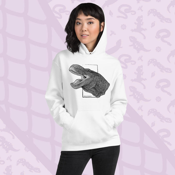 A woman wearing a white hooded sweatshirt with a graphite illustration of a head portrait of a crocodile monitor reptile with its mouth open. The illustration is framed by a white rectangle and the text "Varanus Salvadorii" is below the image. The hoodie has a front pocket.