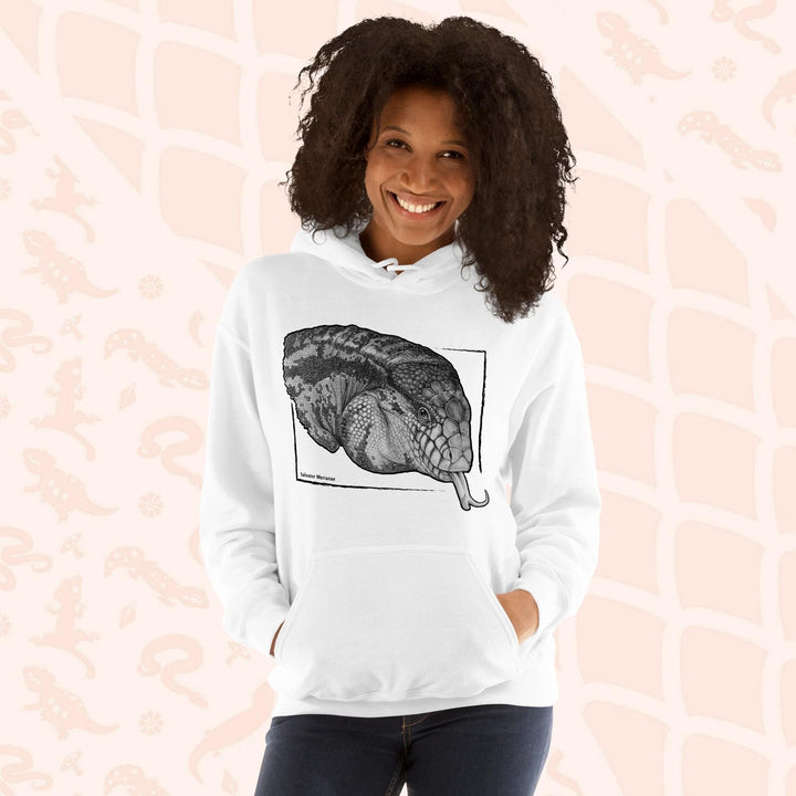 A woman wearing a white hooded sweatshirt featuring a detailed black and white illustration of an Argentine Tegus head with its tongue extended. The artwork is framed within a black rectangle with the reptiles species name of "salvator merianae" on the bottom. The hoodie has a front pocket on it.