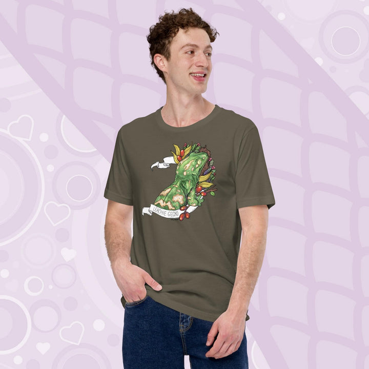 A guy wearing a army green colored tee with a green leachie gecko resting on a log and framed by green leaves and red berries. A white banner frames the reptile with the name "Leachie Gecko" on the bottom.