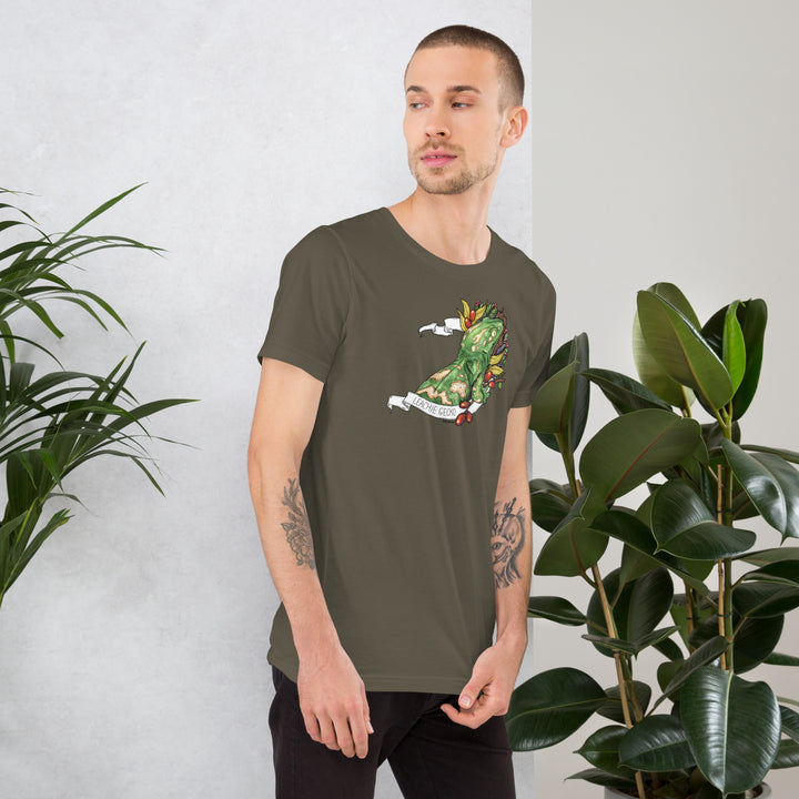 Man wearing a green t-shirt with a graphic of a leachie gecko on it, standing against a white wall with plants.