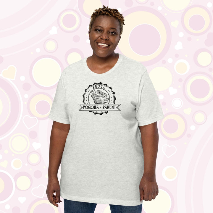 Image of a plus sized woman wearing an ash colored crew neck shirt with a graphic design of a bearded dragon done in black and white centered in a round badge with the text, "Proud Pogona Parent" on the banner design.