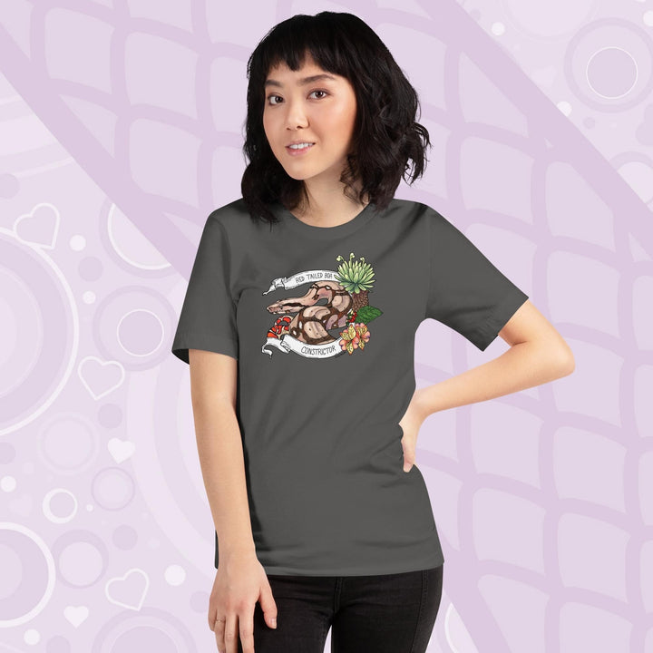 A woman wearing a grey crew necked tee with a graphic of a red-tailed boa constrictor with floral elements and a white banner encircling it. 