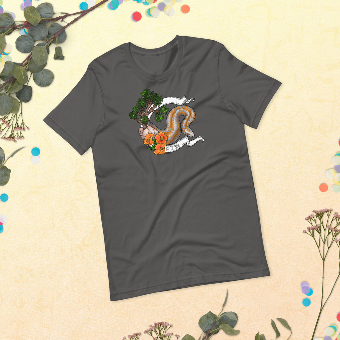 Image depicts a flat lay of a grey shirt with the rosy boa graphic on the front. Leaves and plants are framing around the tee that sits in the center of the image.