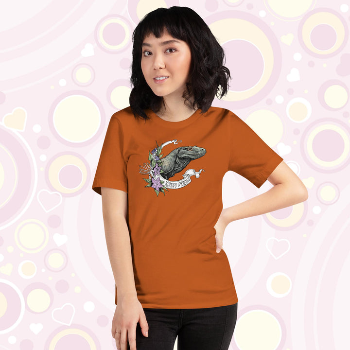 Woman wearing autumn colored crew neck tee with a head shot of a komodo dragon lizard framed by purple flowers and a white banner with text of the animal name.