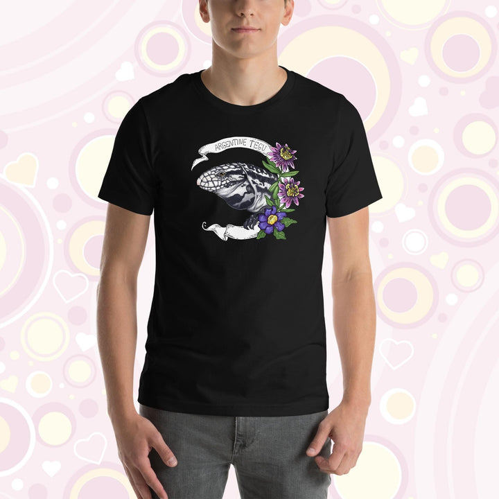 Man wearing black crew neck tee with a hand drawn graphic of an Argentine Tegu lizard. Purple and pink flowers are on the right of the graphic and a white banner encircles the reptile.