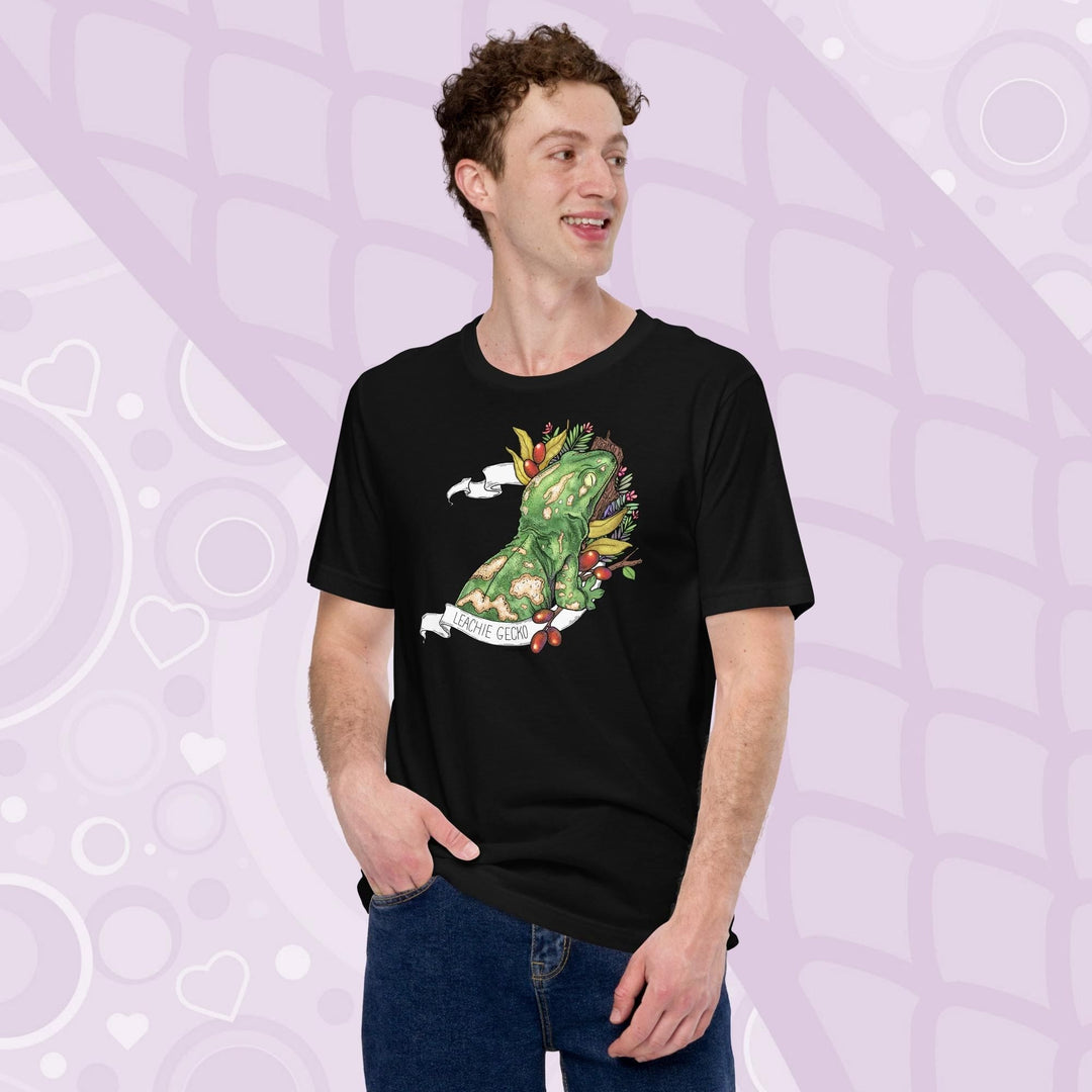 A guy wearing a black colored tee with a green leachie gecko resting on a log and framed by green leaves and red berries. A white banner frames the reptile with the name "Leachie Gecko" on the bottom.