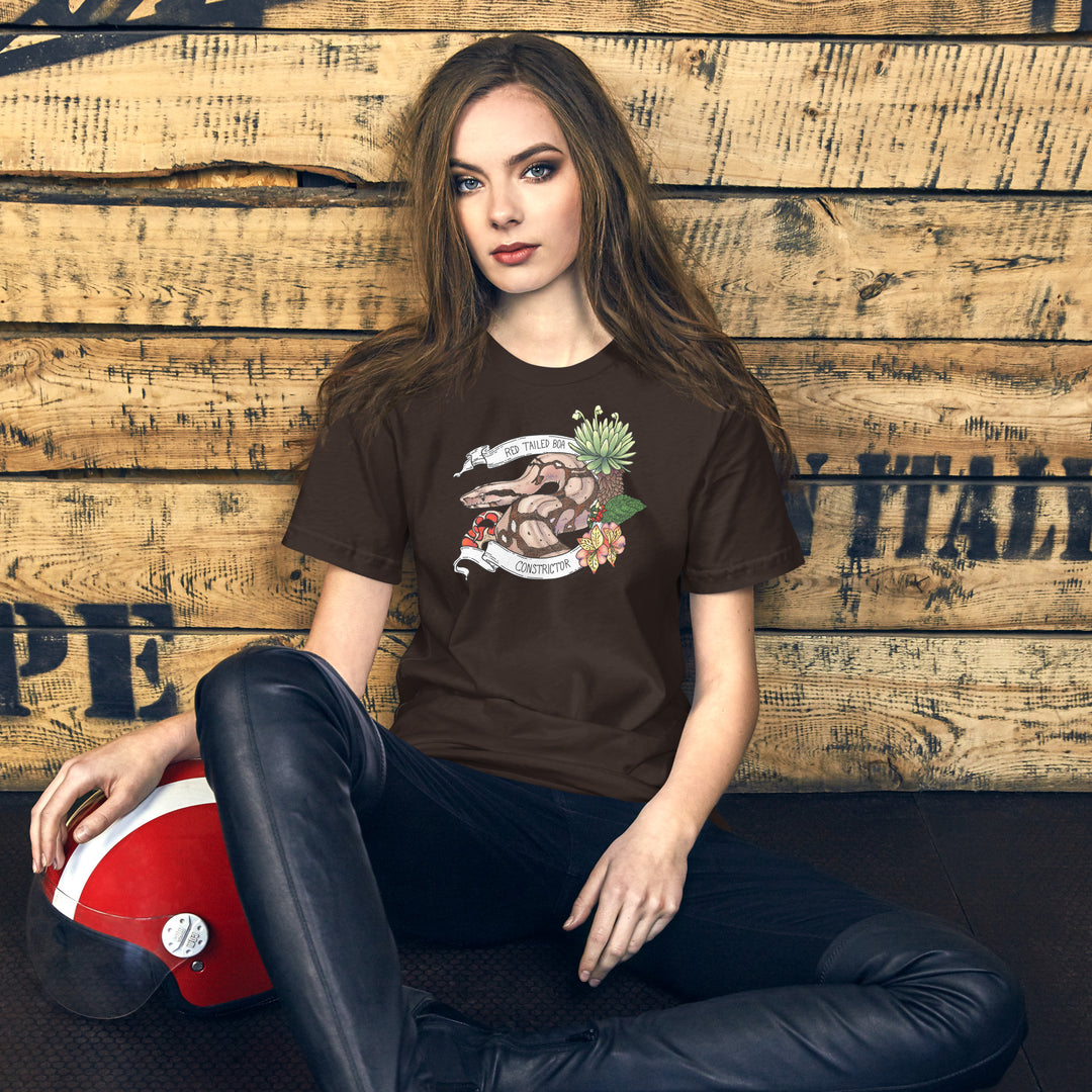 Woman wearing a brown t-shirt with a graphic of a red-tailed boa constrictor, sitting against a wooden wall.