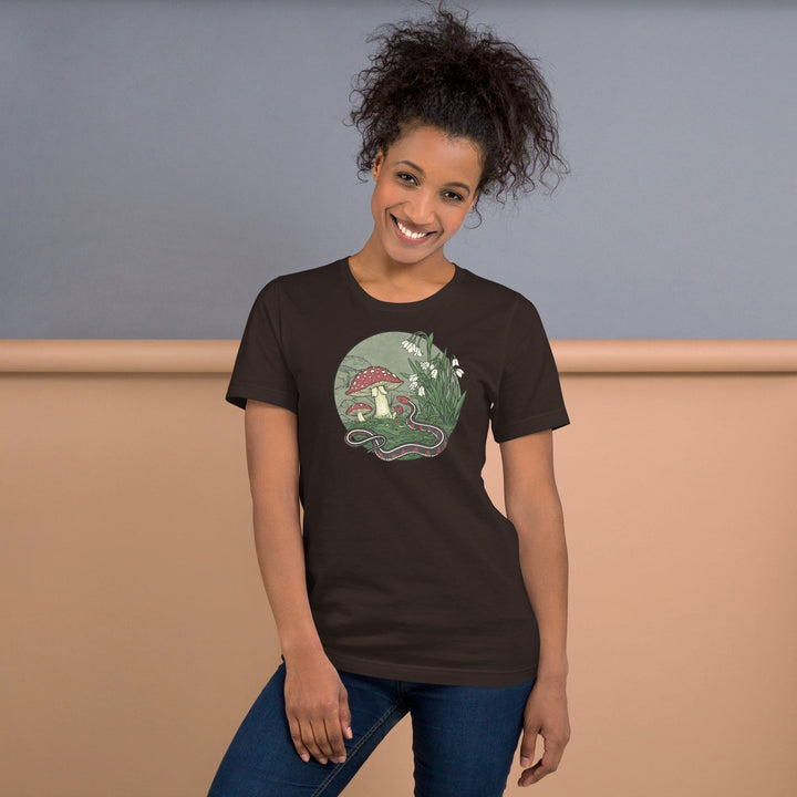 Woman wearing a brown t-shirt with a graphic design of a mushroom and snake, standing against a plain background.