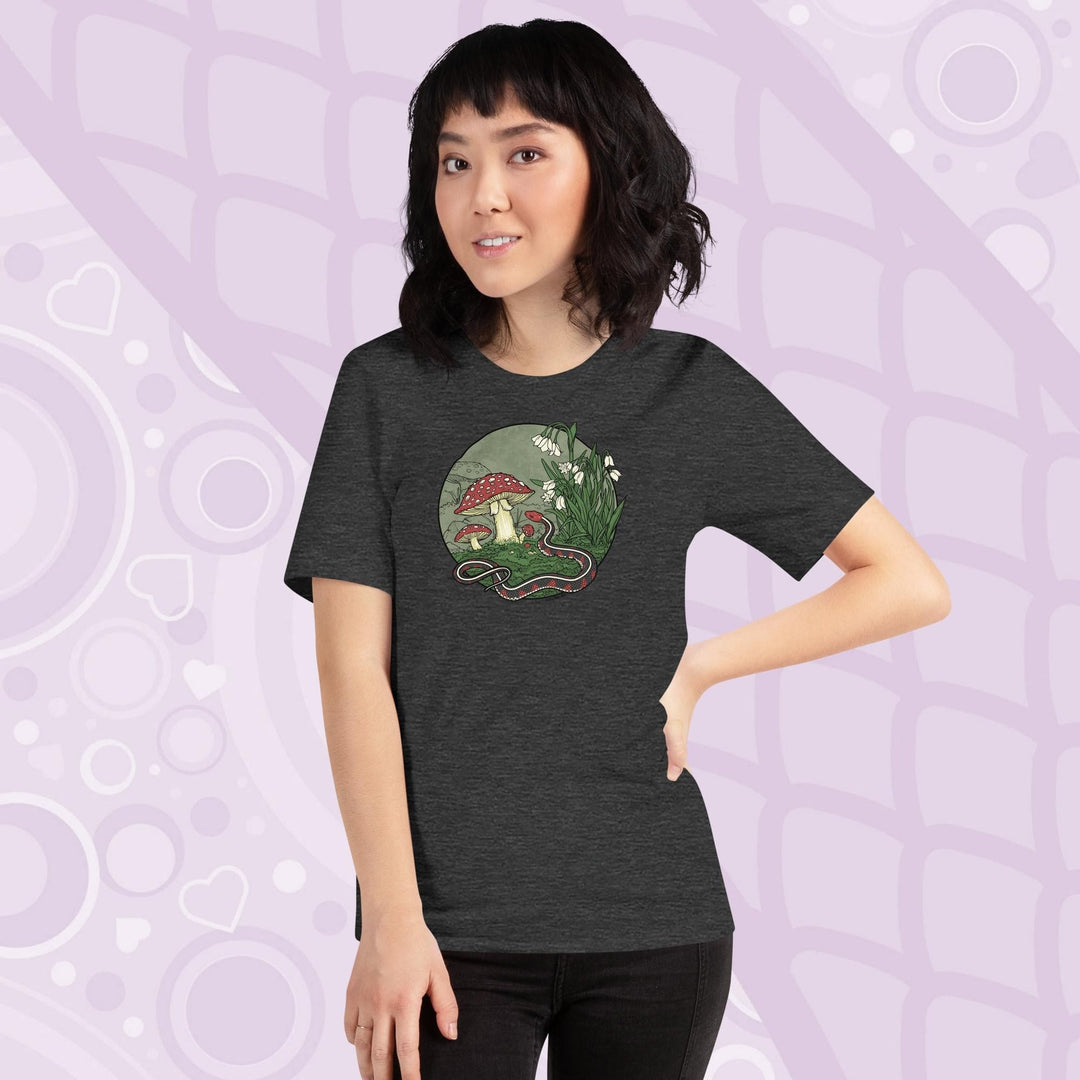 A woman wearing a dark grey tee shirt with a graphic of a red sided garter snake, surrounded by mushrooms and plants with white blossoms. It has simple colors of red, white, and green.  It has lineart outlining the entire illustration.