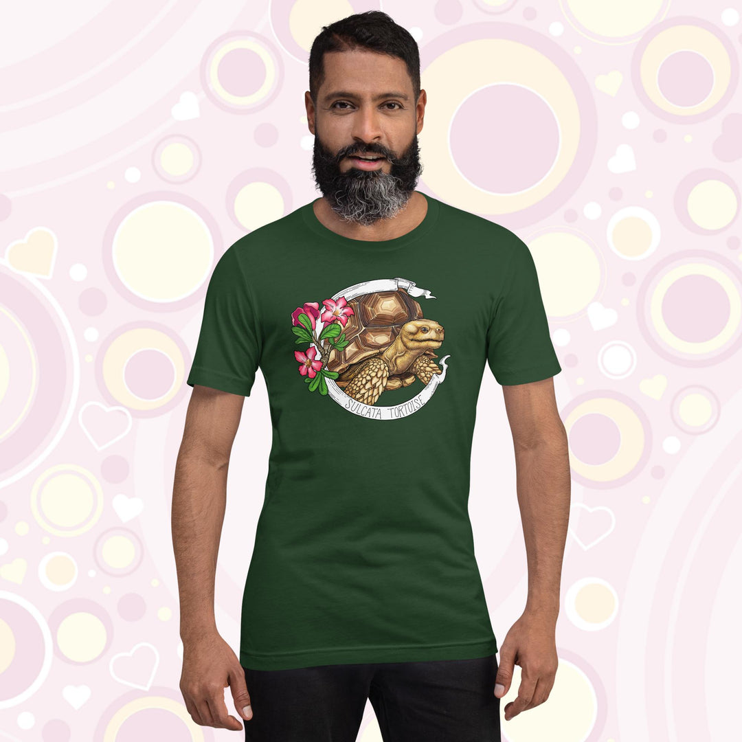 Man wearing forest green crew neck tee shirt with a sulcata tortoise in the middle of a white banner and pink flowers on the left side of the design. The banner reads Sulcata Tortoise.