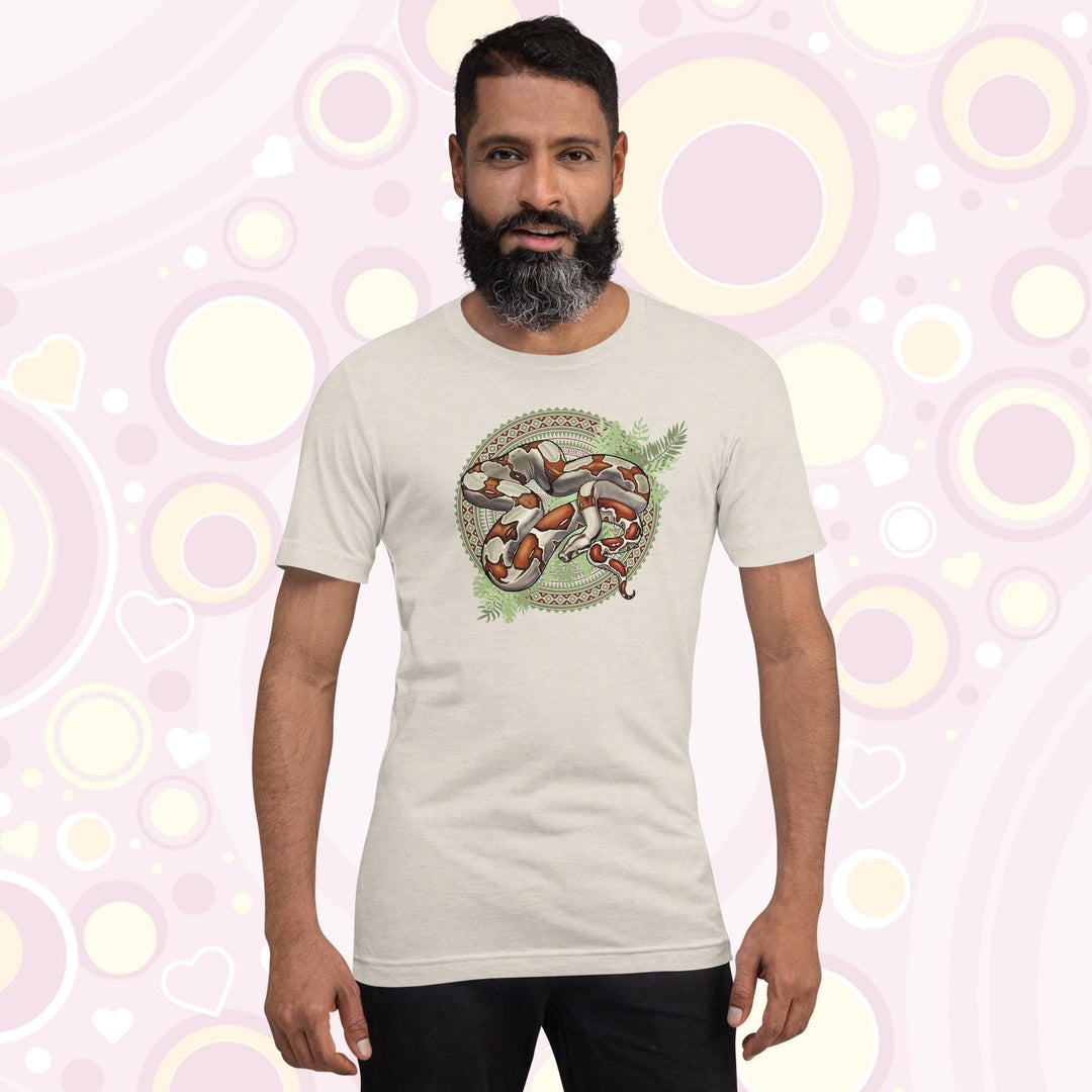 Man wearing heather dust colored crew neck tee showing a red tailed boa constrictor in the center of a westernish patterned design with simple leaf graphics under the boa.